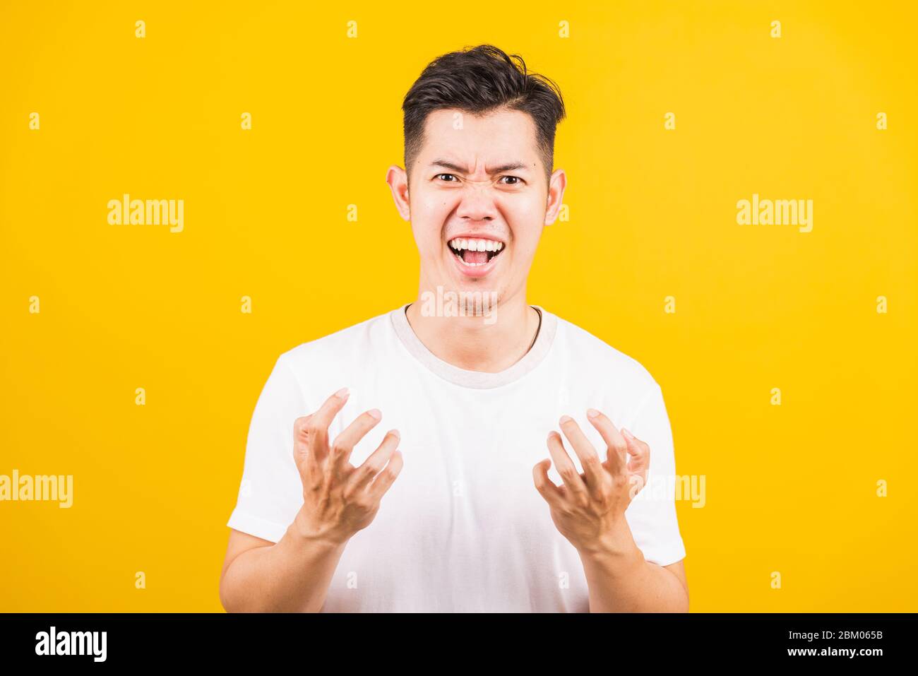 Ritratto Aaian bel giovane uomo in piedi indossando la t-shirt bianca che espressioni irate, faccia arrabbiata urlante, studio girato isolato sfondo giallo Foto Stock