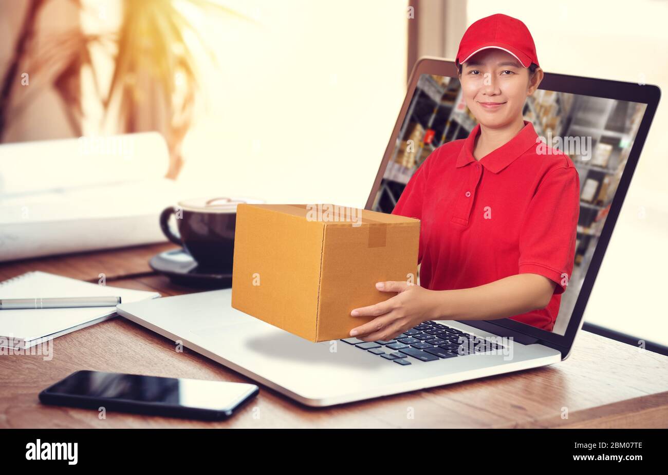 Donna asiatica consegna in camicia rossa con sfondo sfocato magazzino, tenere ordine merci in pacco fuori dal computer portatile. Ordinare online e del Foto Stock
