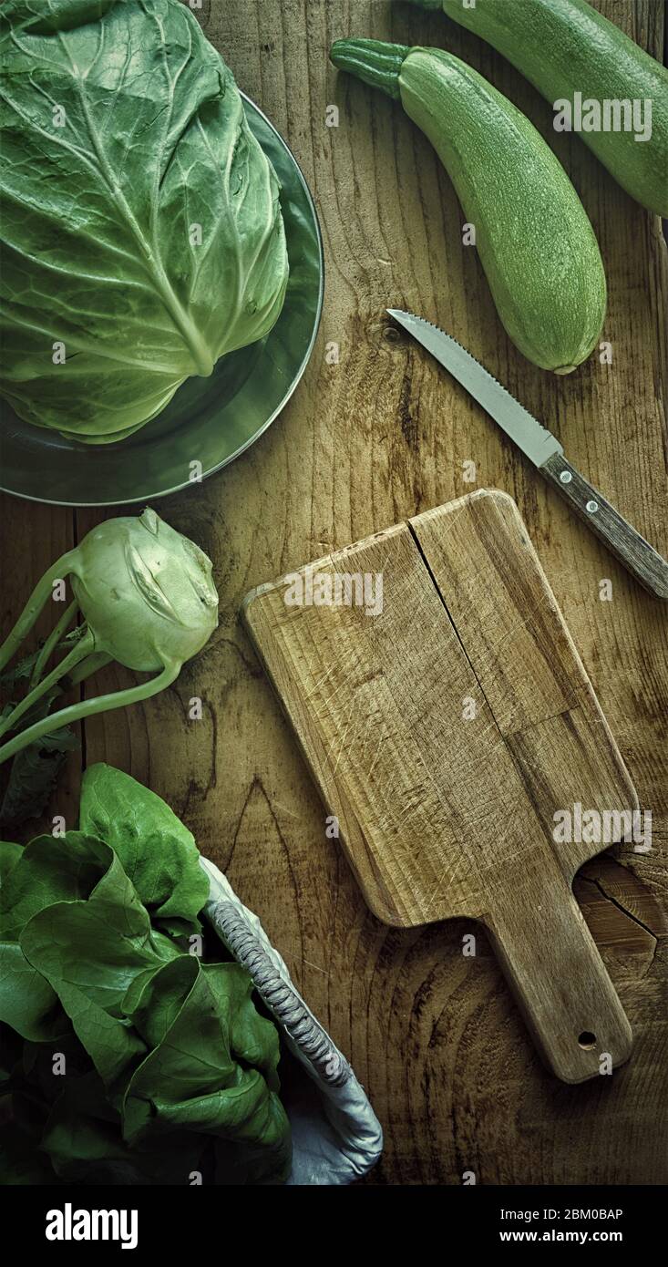 Piatto di verdure fresche verdi kohlrabi rapa cavolo e zucchine su tavola di legno e tagliere in legno mockup in fotografia a bassa luce Foto Stock