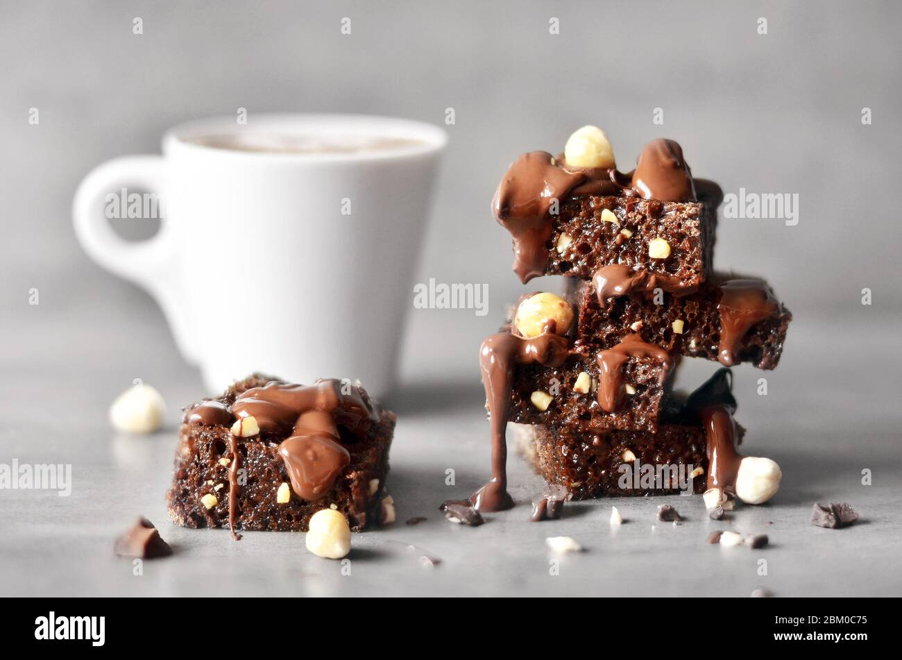 Pila di pezzi di brownie con nocciola e tazza su un tavolo grigio con sfondo grigio. Foto Stock