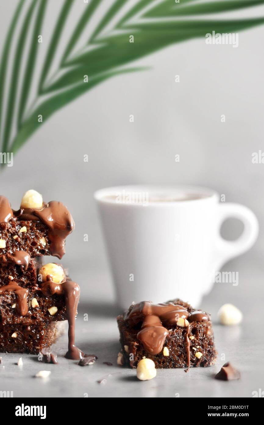 Pila di pezzi di brownie con nocciola, palma e tazza su un tavolo grigio con sfondo grigio. Foto Stock