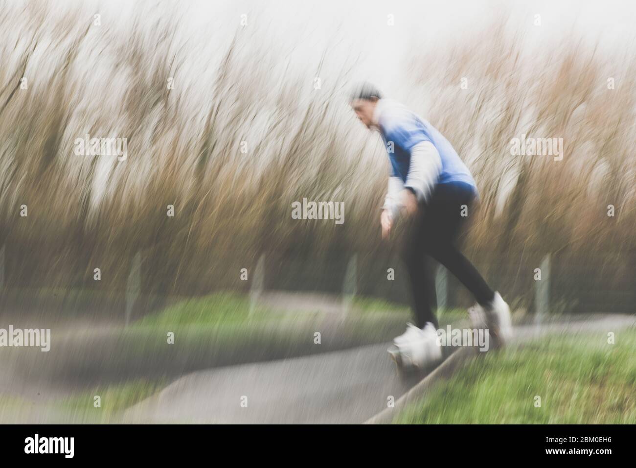 Dal basso, vista laterale di un uomo irriconoscibile e sfocato in un abbigliamento sportivo che corre a bordo di un lungo passerella lungo un pendio che si esibisce in acrobazie nel parco di skate Foto Stock