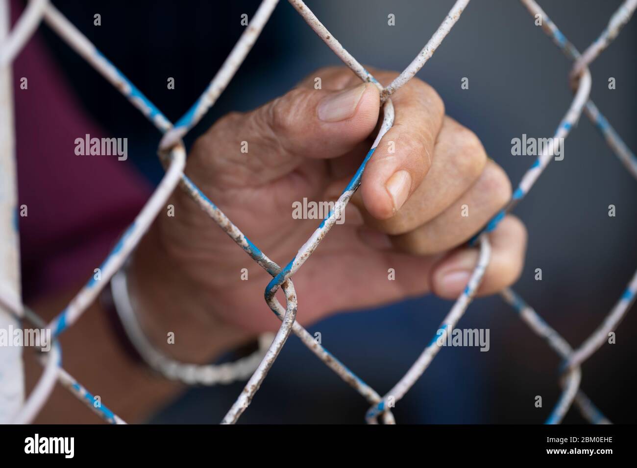 Primo piano della mano di un uomo che tiene su un recinto di filo di ciclone. Forse è incarcerato o bloccato Foto Stock