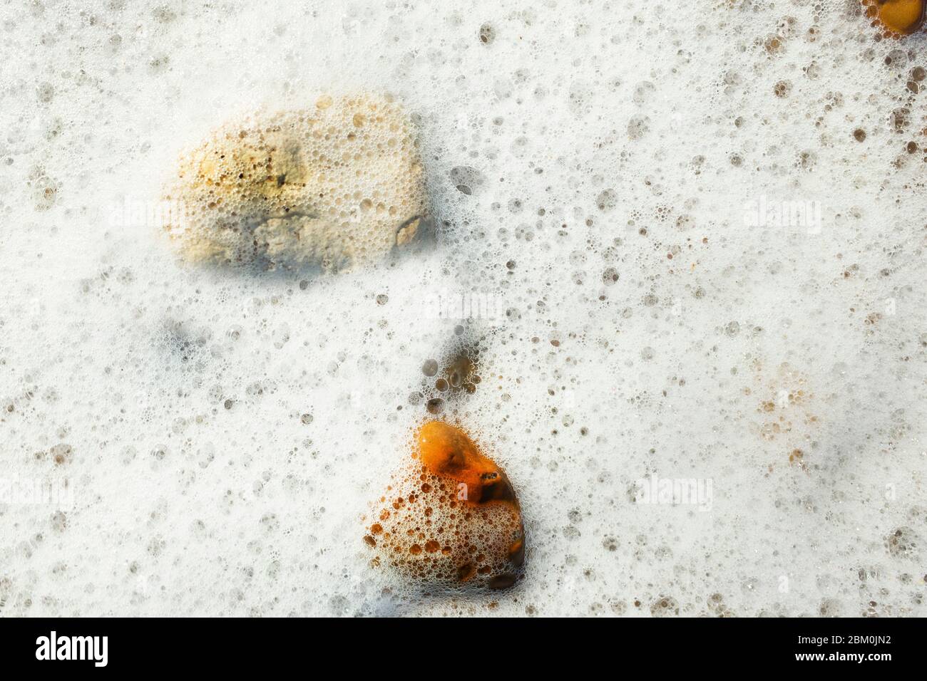 Primo piano immagine di un movimento di acqua di mare che provoca la formazione di schiuma per coprire pietre nel Regno Unito del Kent Foto Stock