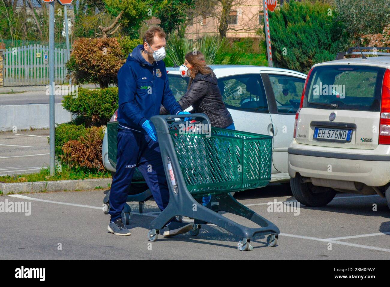 Coppia italiana con maschere di protezione per coronavirus mentre si va per la spesa alimentare. Uomo e donna bianchi con carrelli per lo shopping. Distanza sociale per COVID-19 Foto Stock