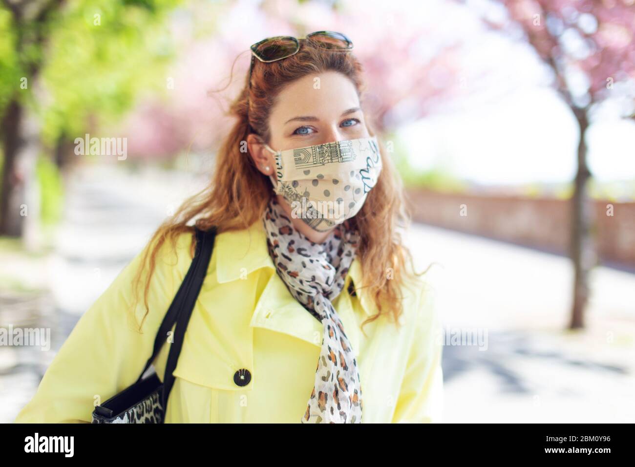 Giovane donna rossa positiva sorridente sotto maschera durante la passeggiata primaverile nel parco Foto Stock