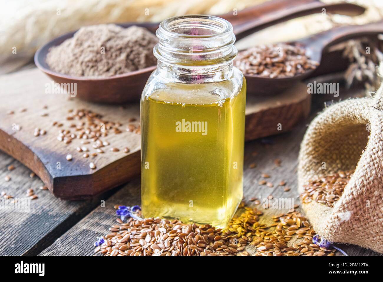 Olio di lino in un vaso vicino ai semi di lino su uno sfondo di vecchi assi. L'olio di semi di lino viene usato in cucina, medicina, cosmetologia. Foto Stock