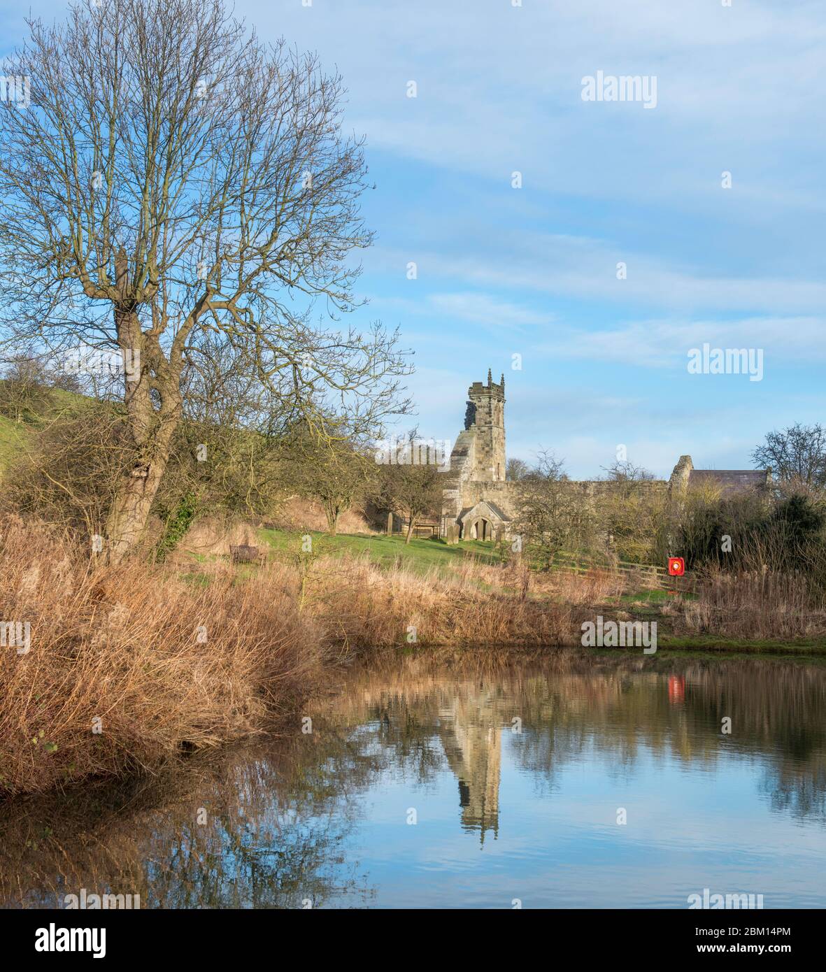 La chiesa in rovina a Wharram Percy deserta borgo medievale si riflette nel laghetto dei pesci Foto Stock