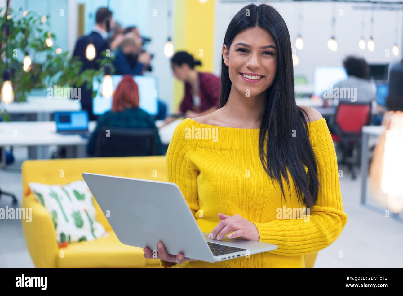 Ritratto di giovane bella ragazza casual felice businesswoman in piedi con il laptop al suo posto di lavoro all'interno di moderno co-working space. Foto Stock