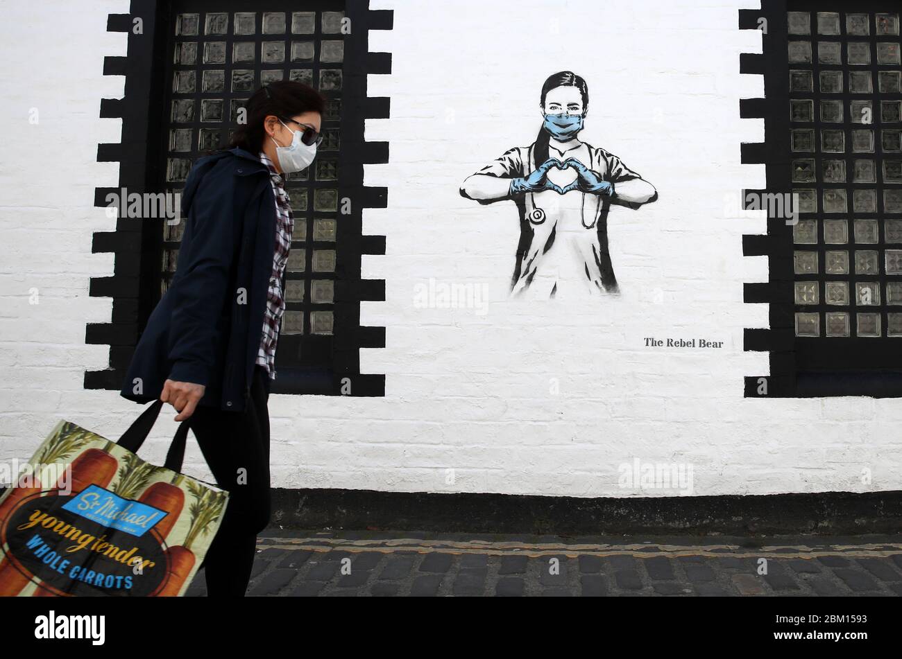 Una persona cammina davanti a un pezzo d'arte dell'artista, conosciuto come l'orso ribelle dopo che è apparso su un muro su Ashton Lane a Glasgow. La nuova aggiunta all'arte di strada di Glasgow sta catturando la crisi globale di Coronavirus. Il pezzo presenta un'infermiera che indossa una maschera e forma un cuore d'amore con le sue mani mentre il Regno Unito continua a bloccarsi per contribuire a frenare la diffusione del coronavirus. Foto Stock