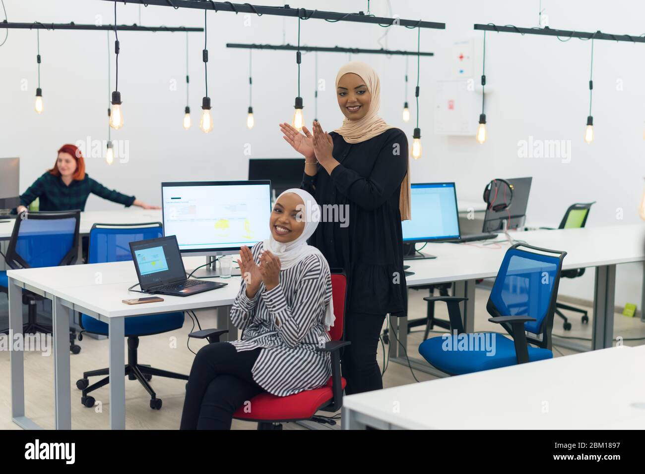 Due allegre e fiduciose donne musulmane africane hijab business applauding e sorridente, il successo e il concetto di successo Foto Stock