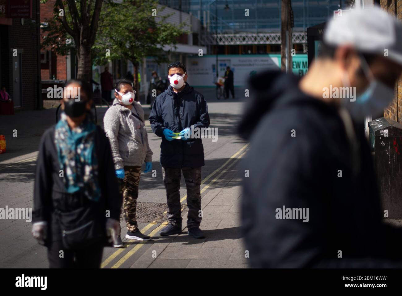 Gli acquirenti che indossano maschere facciali protettive si trovano a 2 m di distanza in coda per una banca di strada alta a East Ham, Londra est, mentre il Regno Unito continua a chiudere a chiave per contribuire a frenare la diffusione del coronavirus. Foto Stock