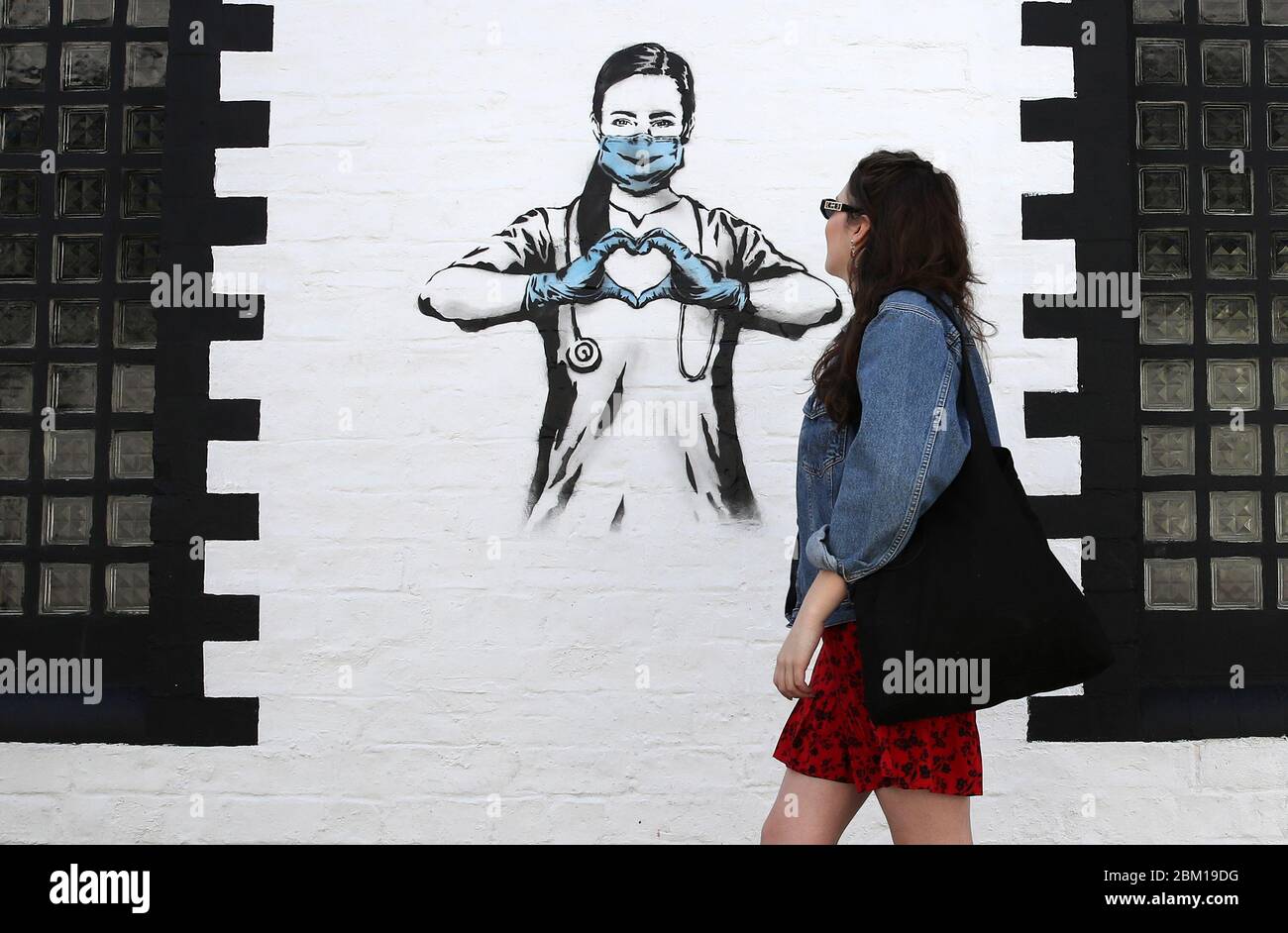 Hannah McGee passa davanti a un pezzo d'arte dell'artista, conosciuto come l'orso ribelle dopo che apparve su un muro di Ashton Lane a Glasgow. La nuova aggiunta all'arte di strada di Glasgow sta catturando la crisi globale di Coronavirus. Il pezzo presenta un'infermiera che indossa una maschera e forma un cuore d'amore con le sue mani mentre il Regno Unito continua a bloccarsi per contribuire a frenare la diffusione del coronavirus. Foto Stock