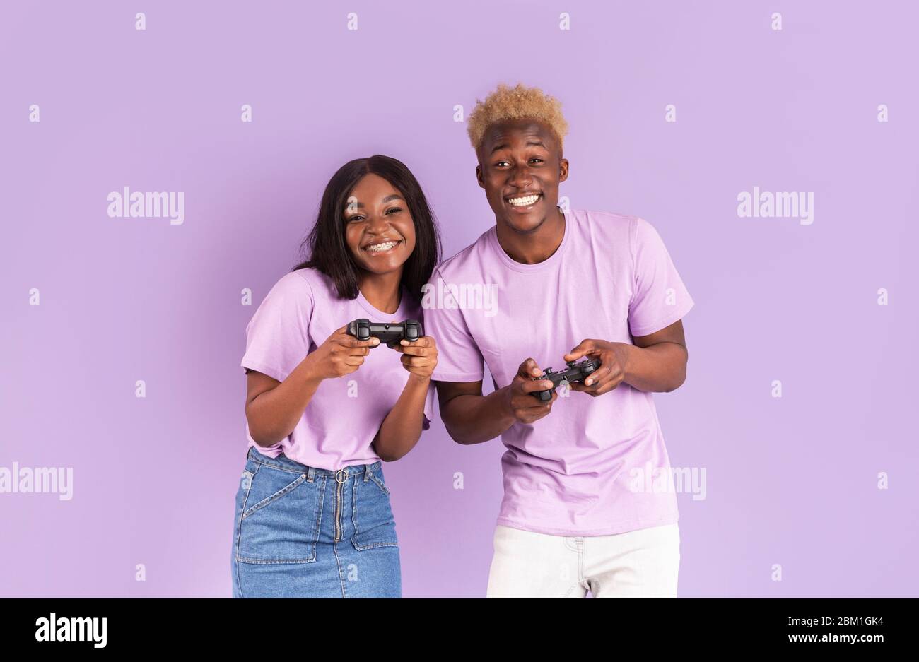 Felice coppia Africano-americana con joystick che giocano a videogiochi su sfondo lilla Foto Stock