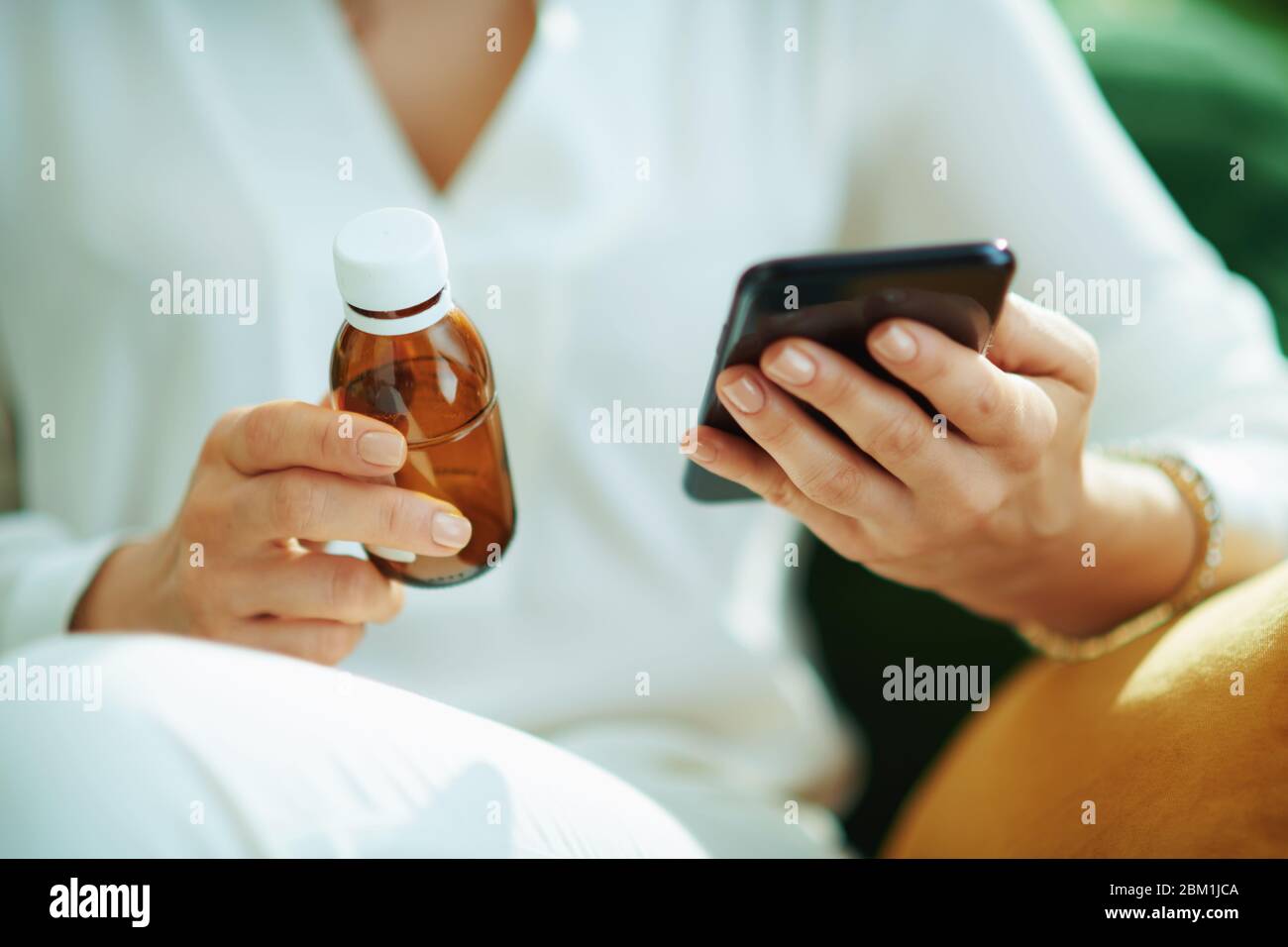 Primo piano su donna con flacone di medicina vuoto ordinare online farmaci su uno smartphone in casa in giorno di sole. Foto Stock