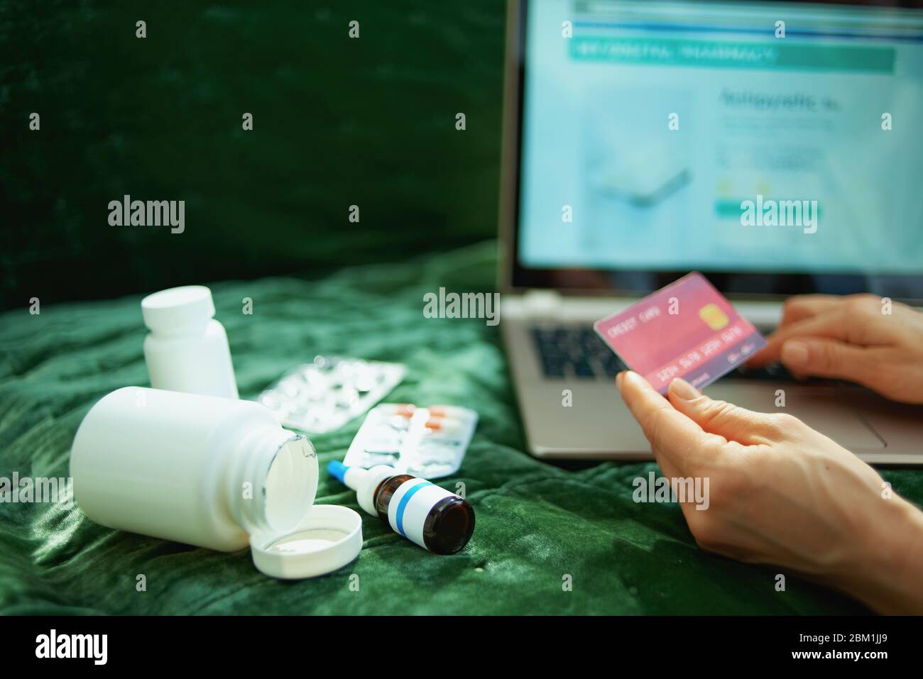 Primo piano su donna con carta di credito e bottiglia di medicina vuota che ordina online farmaci su un portatile a casa in giorno di sole. Foto Stock