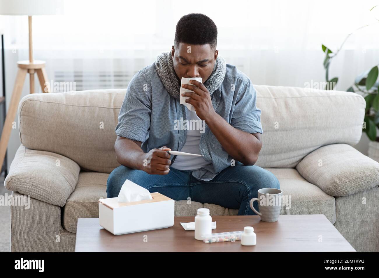 Influenza stagionale. Malato Afro Guy controllo della sua temperatura corporea a casa Foto Stock