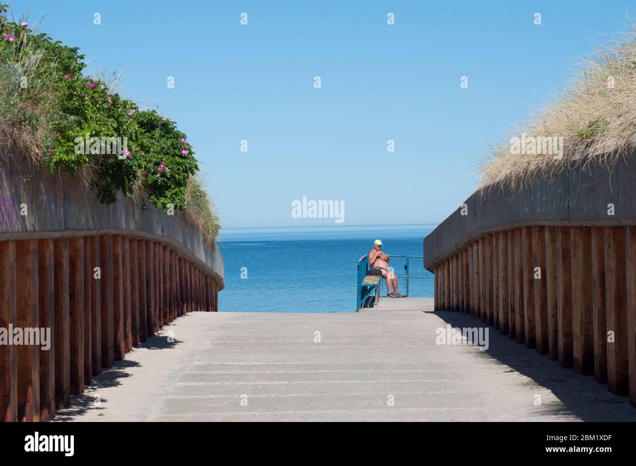 Uomo anziano seduto su una sedia a sdraio su una spiaggia estiva vuota in una giornata calda Foto Stock