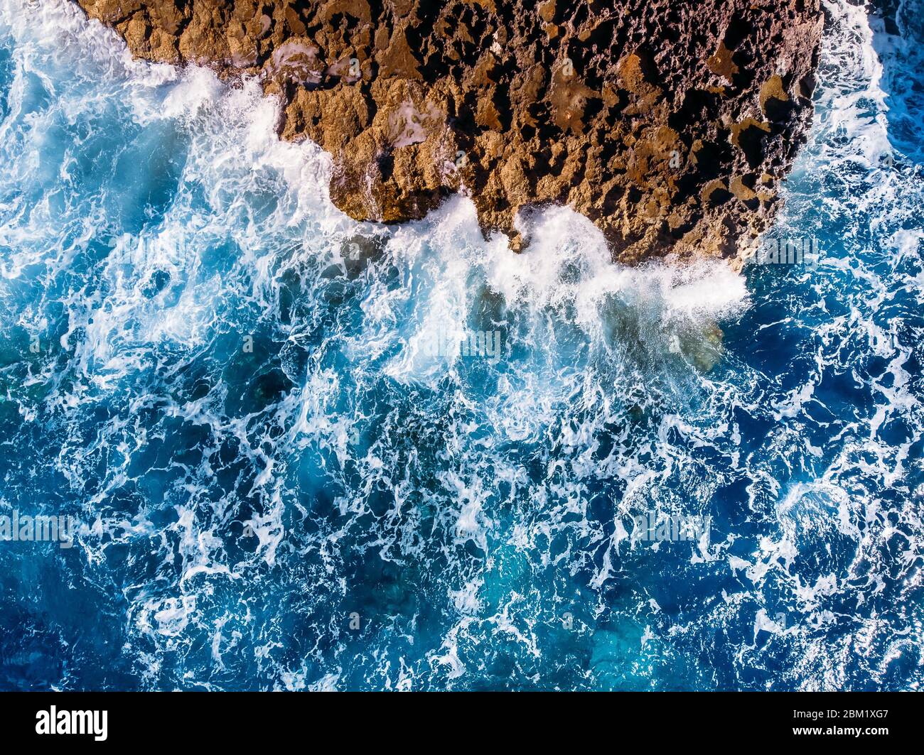 Vista dall'alto mare azzurro con onde che battono sulla spiaggia e sulle rocce. Foto aerea. Foto Stock