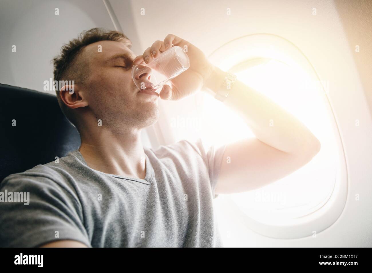 L'uomo beve acqua in un aereo prima del decollo. Concetto mette le orecchie Foto Stock