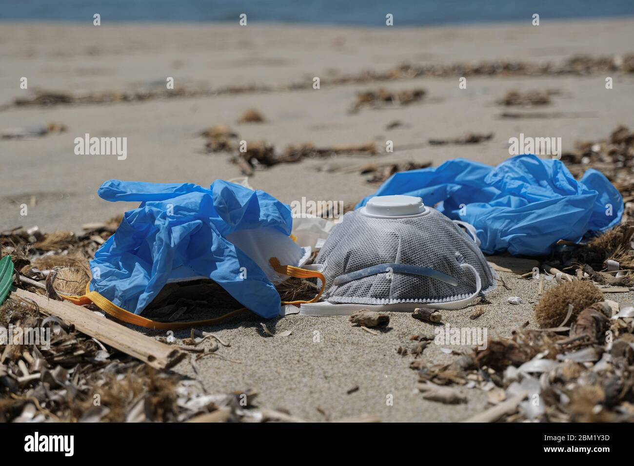 Maschera anti-virus protettiva FFP e guanti di plastica spazzatura sulla costa sabbiosa del mare, malattia da inquinamento da cocvidi coronavirus Foto Stock