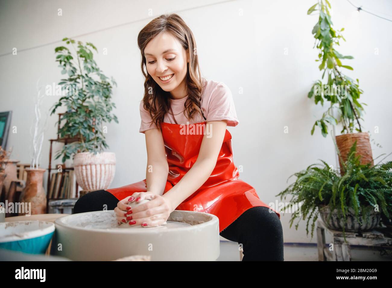 Ruota per vasaio da lavoro. Giovane donna felice in grembiule rosso scolpisce da argilla Foto Stock