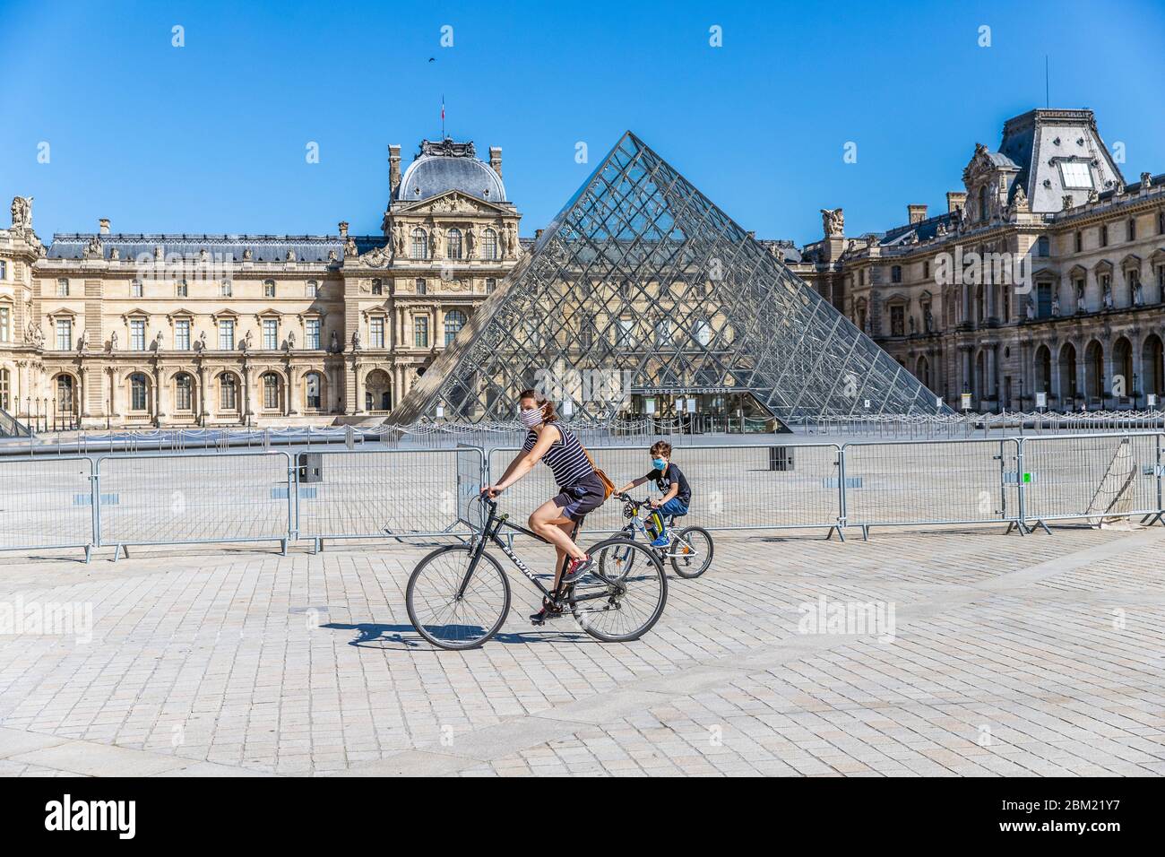 Una mamma e il suo bambino in bicicletta di fronte alla piramide del Louvre a Parigi durante il blocco Coronavirus covid-19 Foto Stock