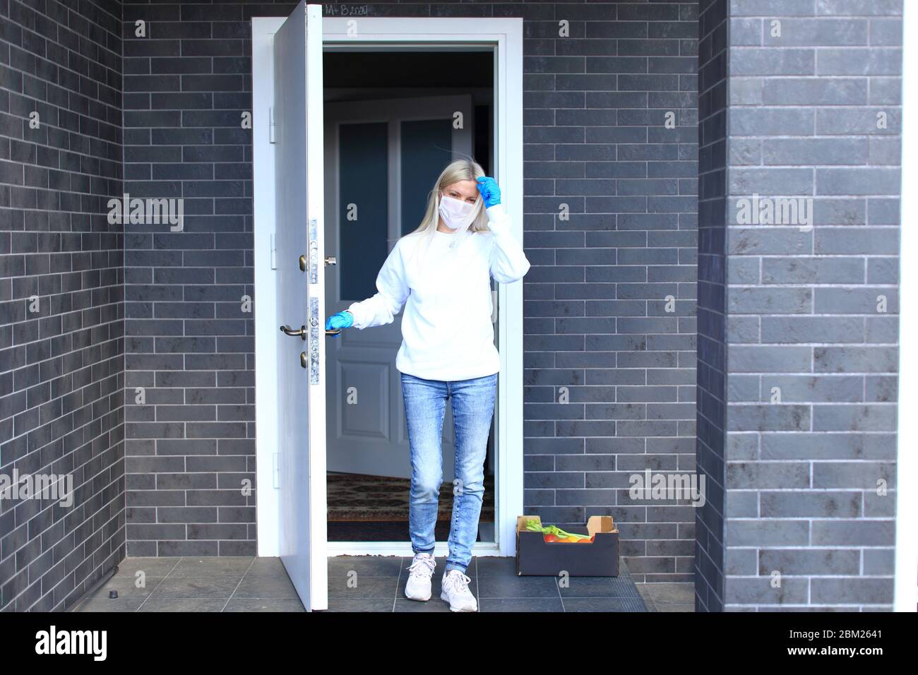 Una giovane ragazza sta in piedi sul portico della sua casa in una maschera respiratoria. Foto Stock