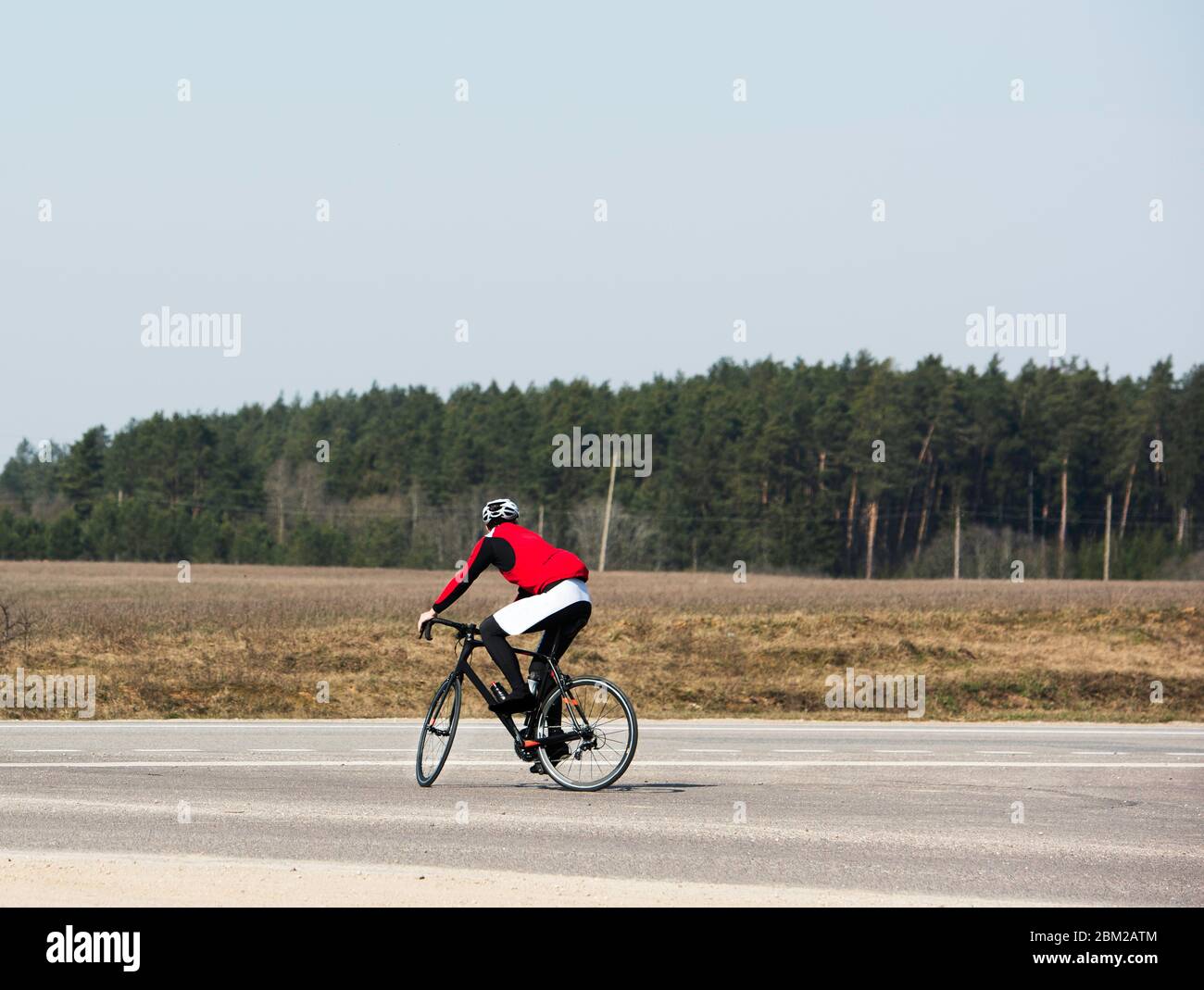 Gioioso ciclista maschile in bicicletta su strada vuota durante il coronavirus (COVID-19) pandemico di blocco, attraversando la strada, godendo la vista, copia spazio. ATH Foto Stock