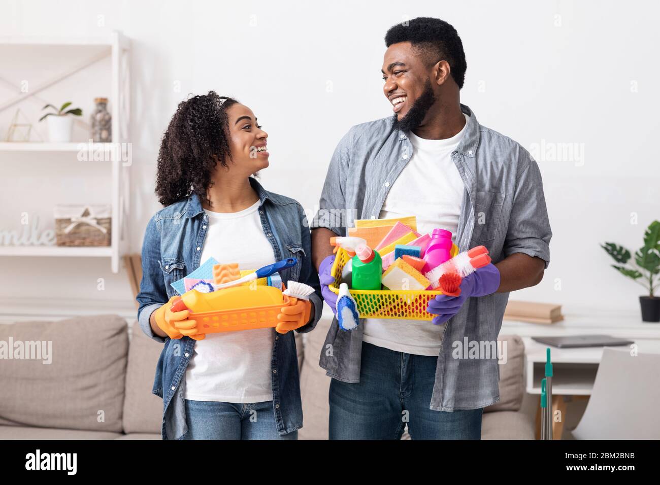 Grande giorno di pulizia. Contenitori di tenuta per coppia nera sorridente con utensili per la casa Foto Stock