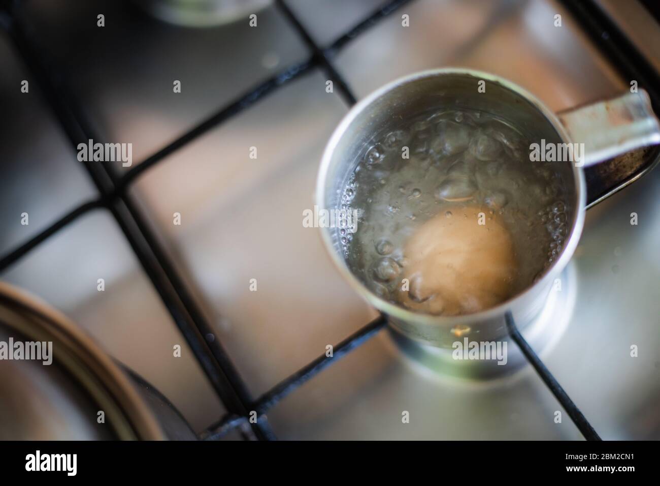 Uova sode nel mestolo di acqua sul fornello da cucina Foto stock - Alamy