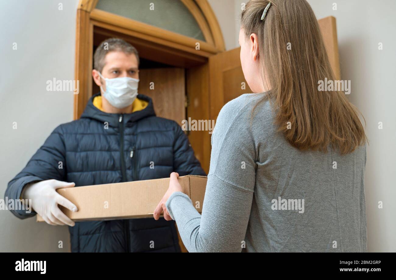 Corriere maschile in maschera medica e guanti consegna pacco. Foto Stock