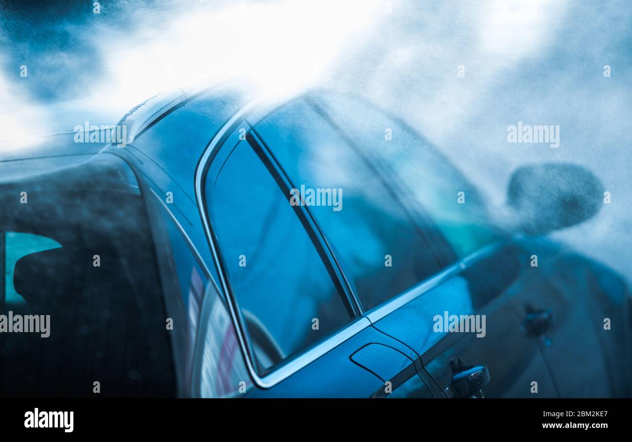 Primo piano dell'auto nera da passeggeri spruzzata e risciacquata e durante la guida attraverso il servizio di autolavaggio automatico. Foto Stock