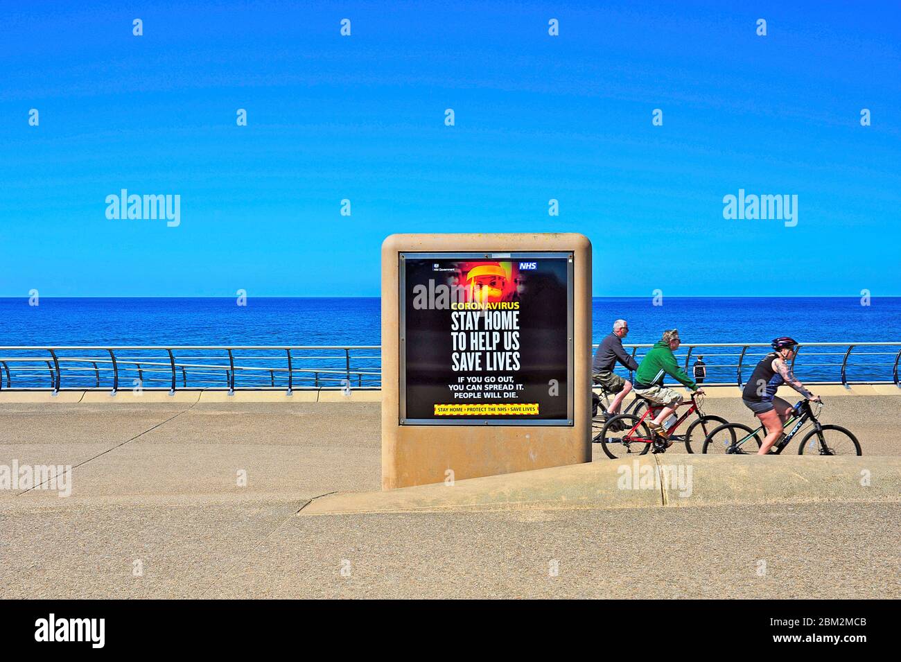 Rimani a casa per salvare vite segno sul lungomare di Blackpool in una calda giornata di primavera soleggiato con tre ciclisti che fanno esercizio quotidiano Foto Stock