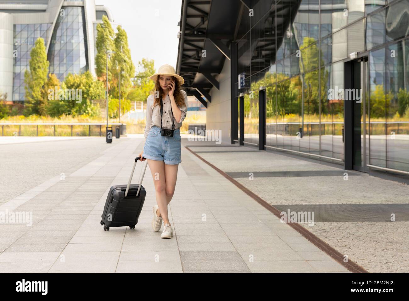 Immagine di giovane eccitato bella donna in posa turistica. Una donna con una valigia si trova alla stazione, comunica con qualcuno al telefono. Foto Stock