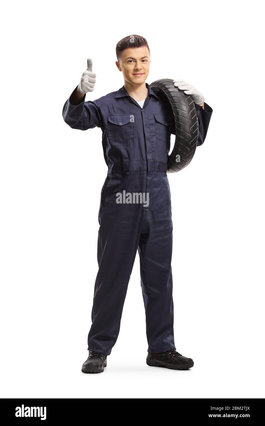 Ritratto a tutta lunghezza di un giovane meccanico che trasporta un pneumatico da moto e mostra pollici isolati su sfondo bianco Foto Stock