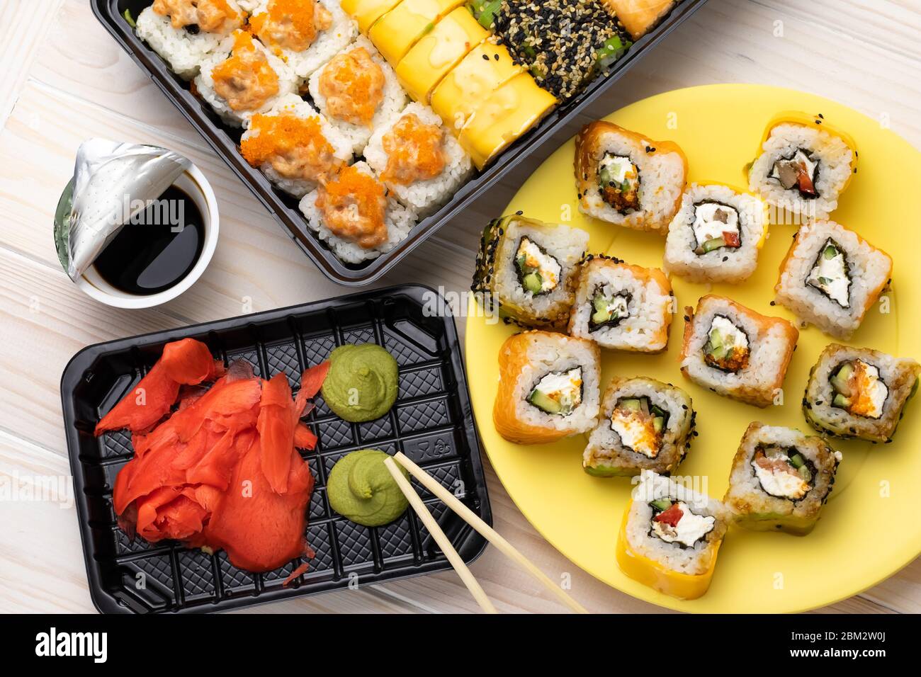 Sushi, verdure crude avvolte in alghe. Rotoli su piatto giallo con wasabi e salsa di soia su sfondo legno. Un piatto giapponese di pesce con ch Foto Stock