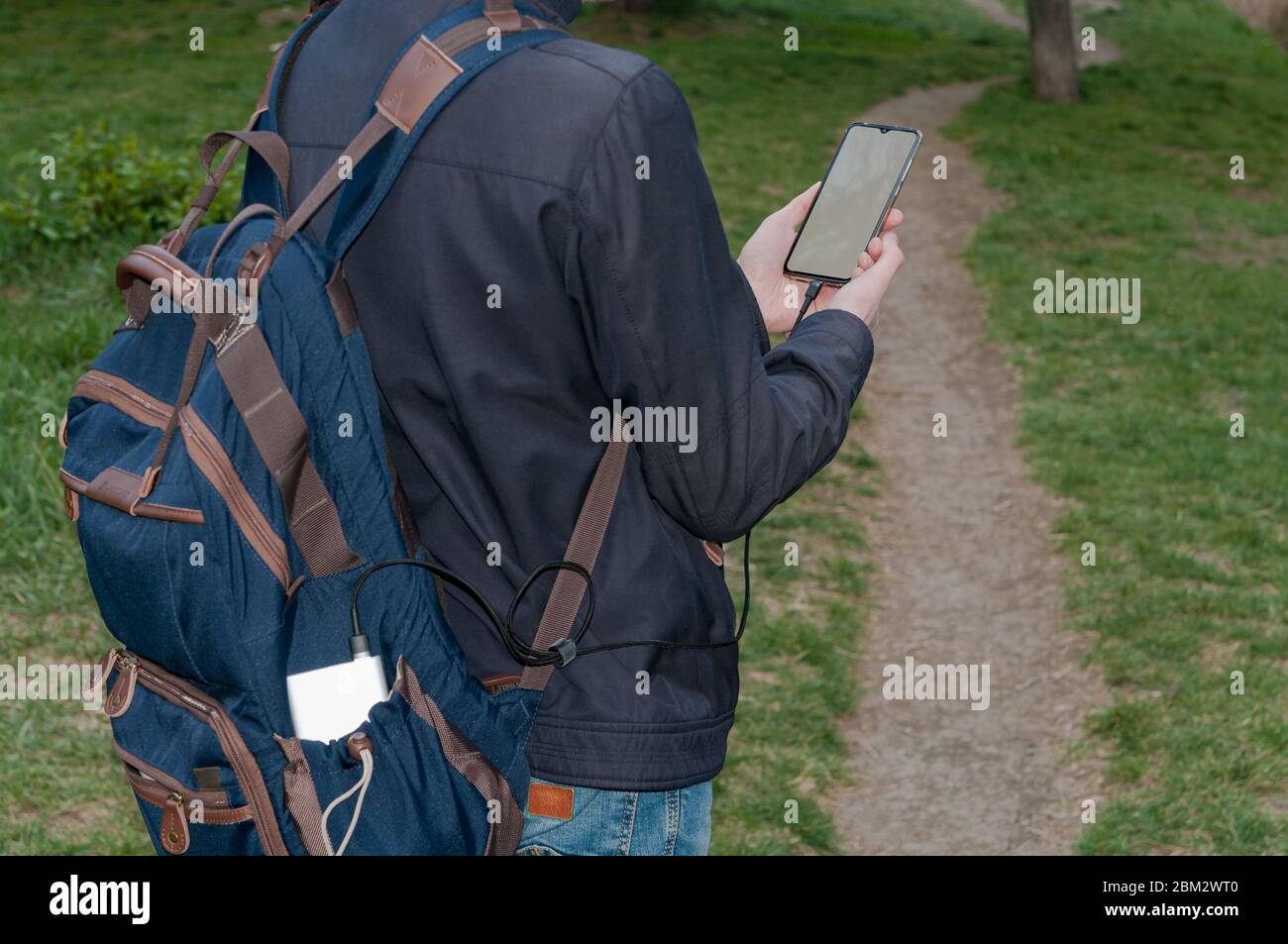 Uomo che tiene e utilizza uno smartphone con ricarica su schermo bianco dal power bank all'aperto con sfondo naturale Foto Stock