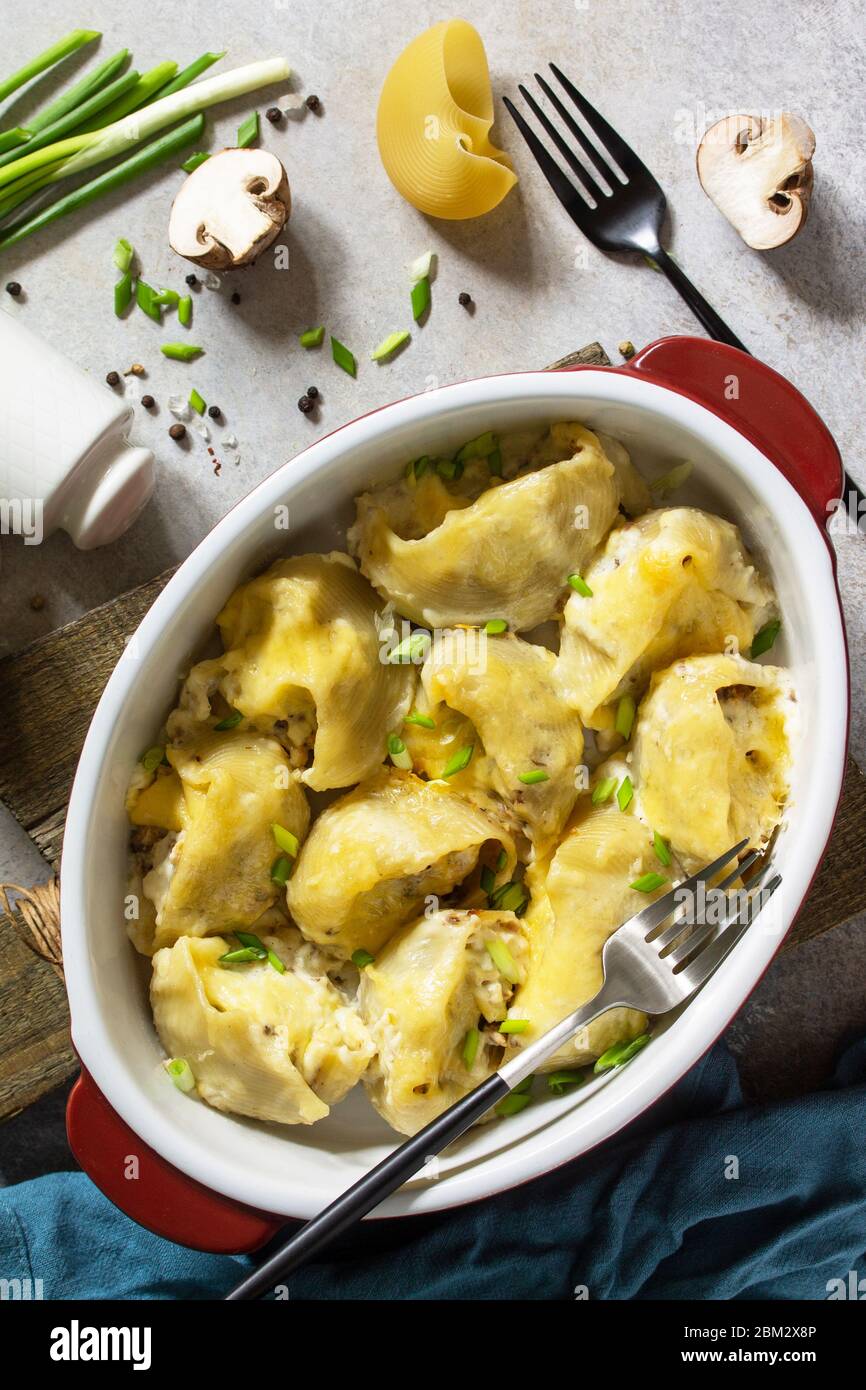 Pasta italiana Conchiglioni rigati ripieni di pollo, champagne reali, cotti con formaggio in salsa di bechamel su un piano in pietra grigia. Vista dall'alto fl Foto Stock