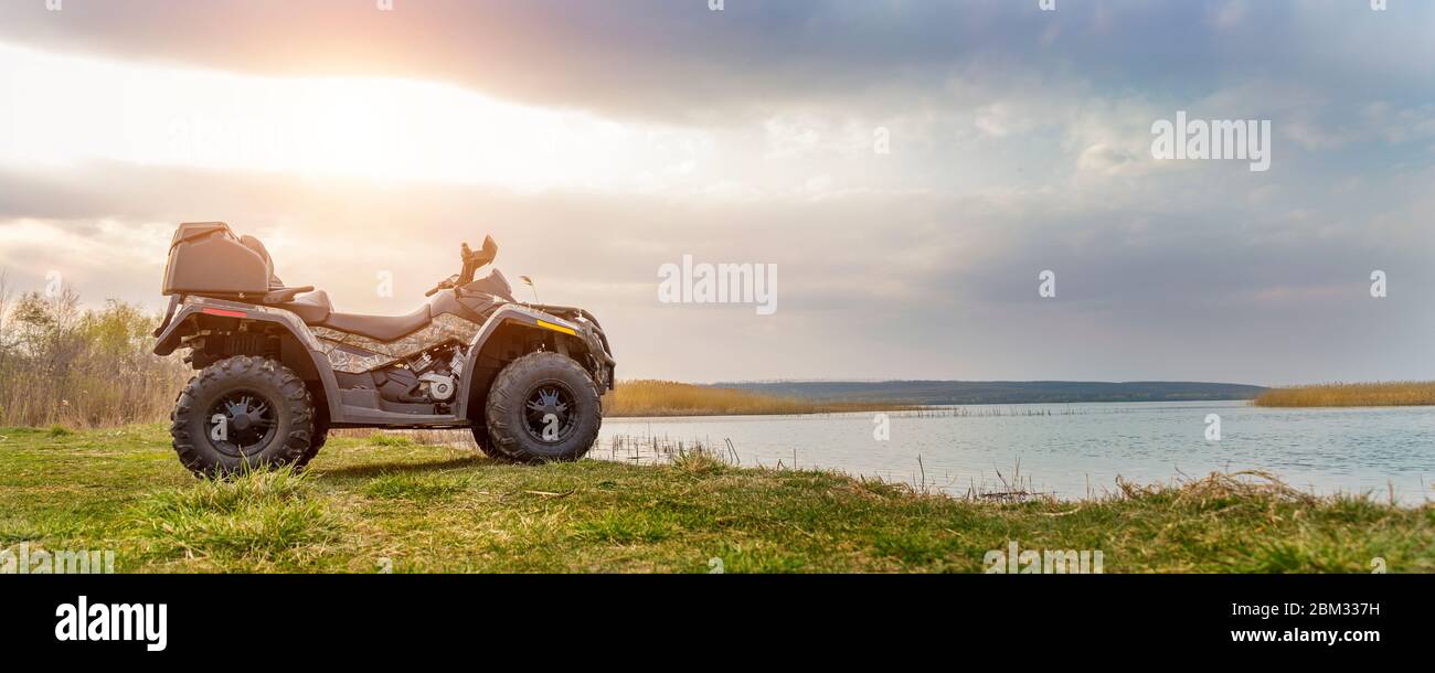 ATV awd quad moto pov vista vicino lago o fiume stagno costa con bella natura paesaggio e cielo sfondo nuvoloso. Avventura fuoristrada Foto Stock