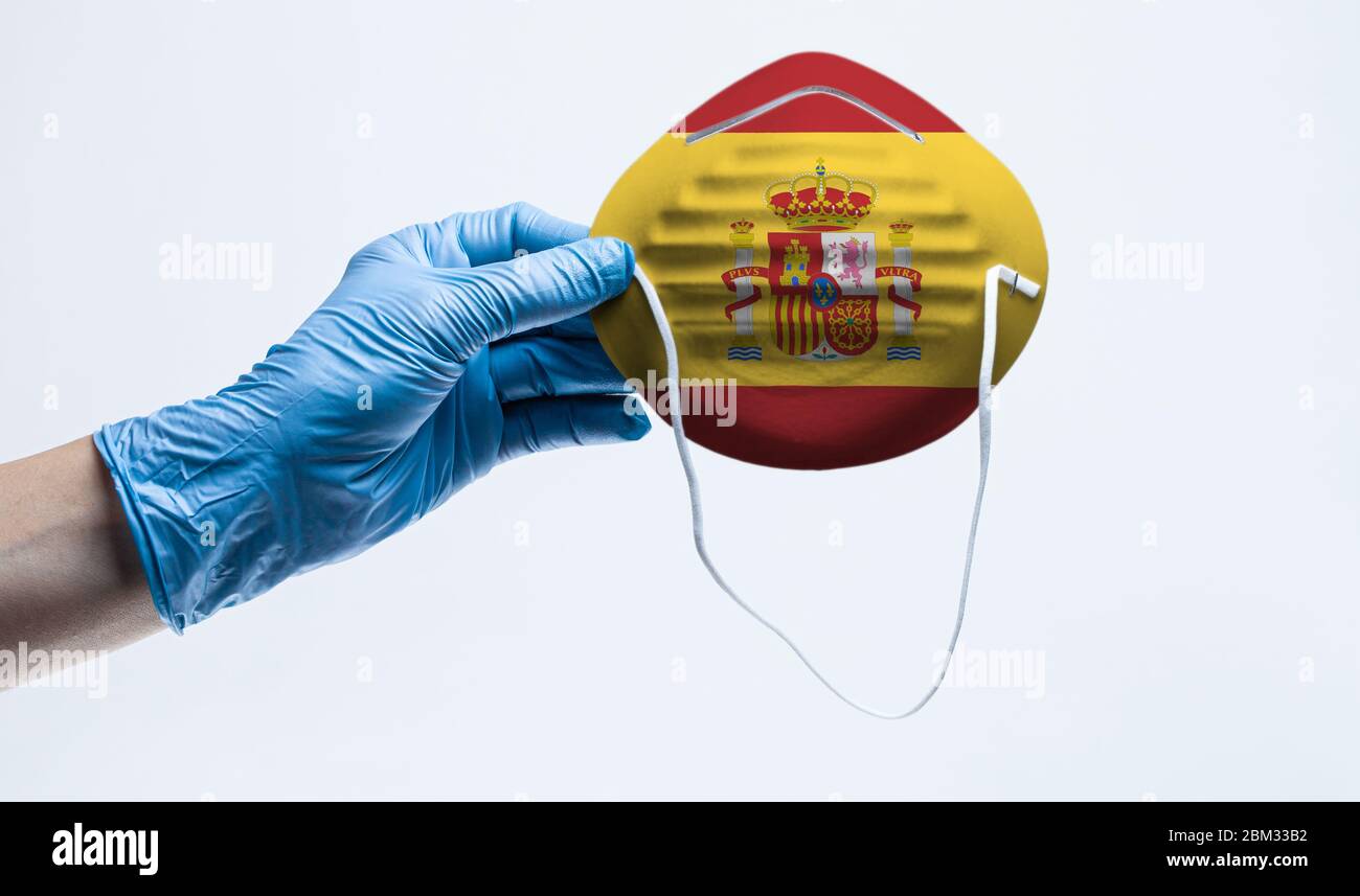 La mano con guanto chirurgico regge la maschera protettiva con bandiera spagnola. Concetto di virus corona diffuso in Spagna. Foto Stock
