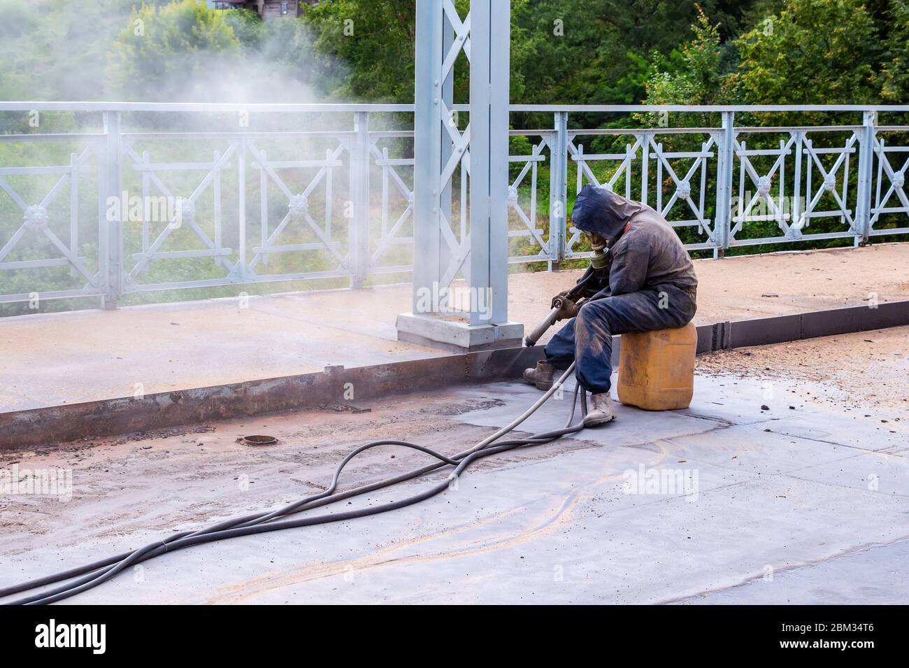 Lavoratore con maschera protettiva funziona un ponte con sabbiatura. Il processo di sabbiatura Foto Stock