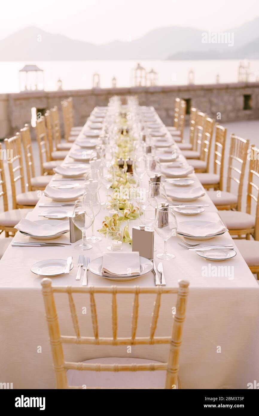 Prospettiva tavolo da pranzo per matrimoni vista ricevimento. Un lungo tavolo rettangolare con tovaglia color crema e fiori di orchidea al centro. Sullo sfondo Foto Stock
