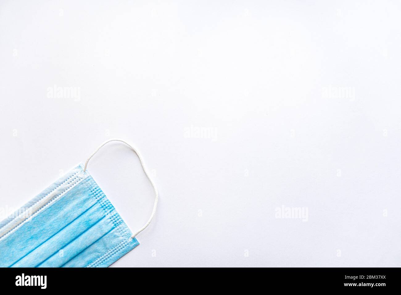 Maschera protettiva monouso blu per uso medico su uno spazio di copia su sfondo bianco. Una medicazione chirurgica chiude la bocca e il naso. Sanità, medicina, covid Foto Stock