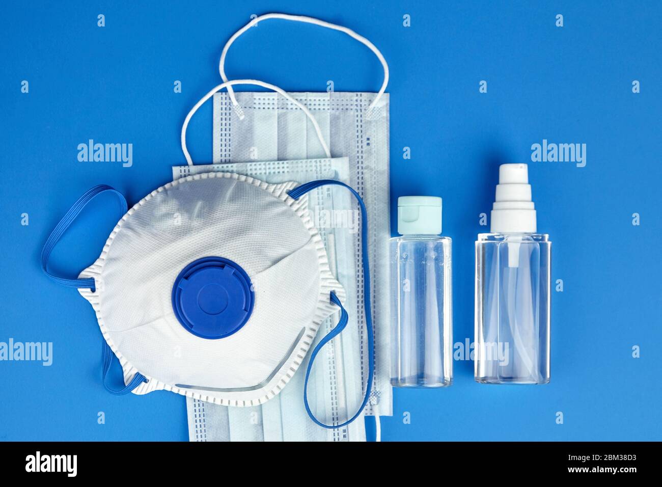Respiratore per facciali filtranti N95, maschere chirurgiche monouso, flaconi di igienizzante antibatterico per mani (gel antisettico alcolico) su fondo blu, a. Foto Stock