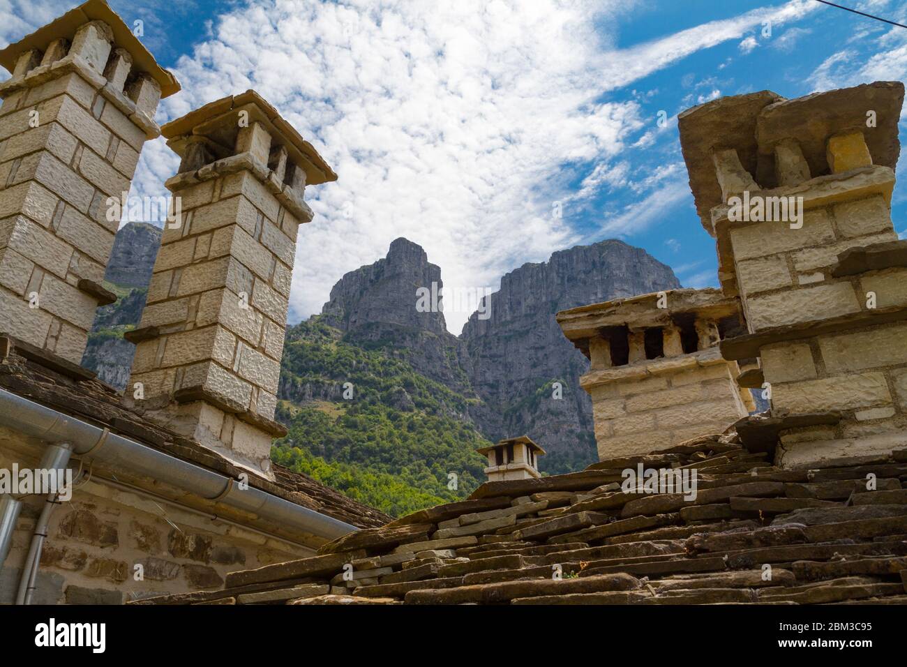 Vista delle torri di Astraka (montagna Tymfi) a Mikro Papigo, Grecia. Camini e tetti realizzati in pietra in primo piano e le torri in background. Foto Stock