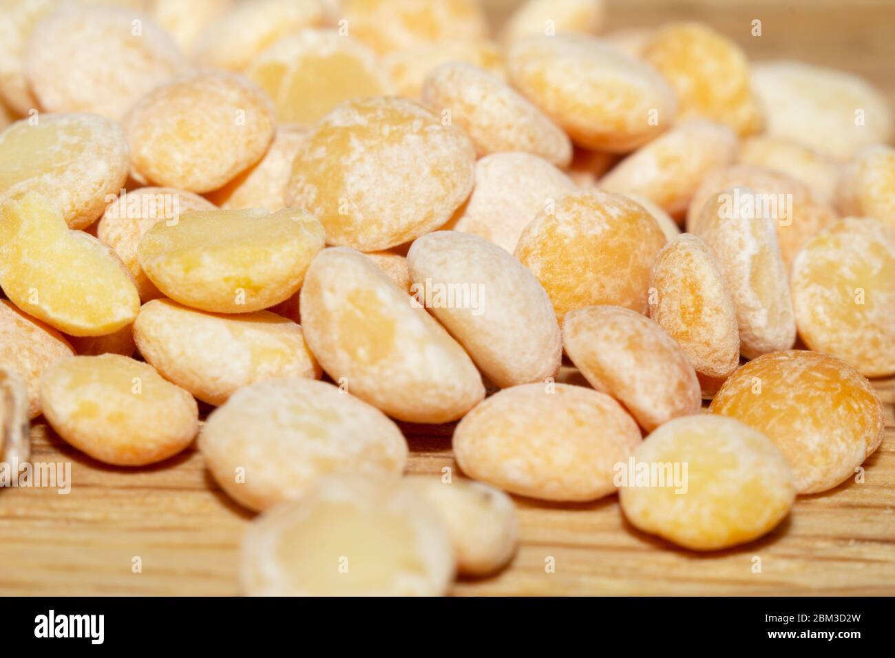 Piselli spezzati crudi di varietà gialla sulla superficie di legno e sparsi accanto, primo piano in selective focus. Cibo vegano, foto di scorta Foto Stock