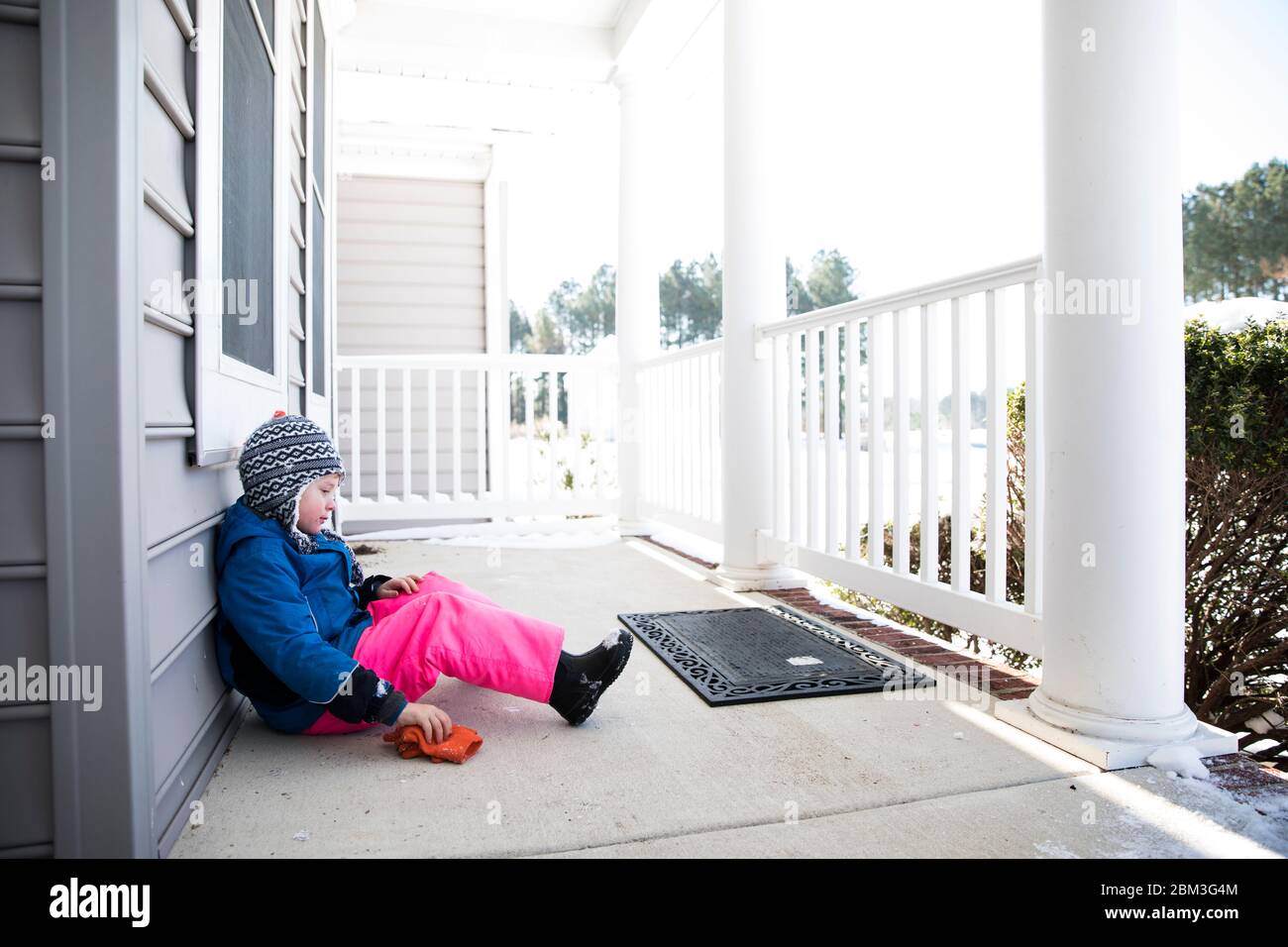 Ampia vista del ragazzo in pantaloni da neve rosa seduti Portico anteriore innevato Foto Stock