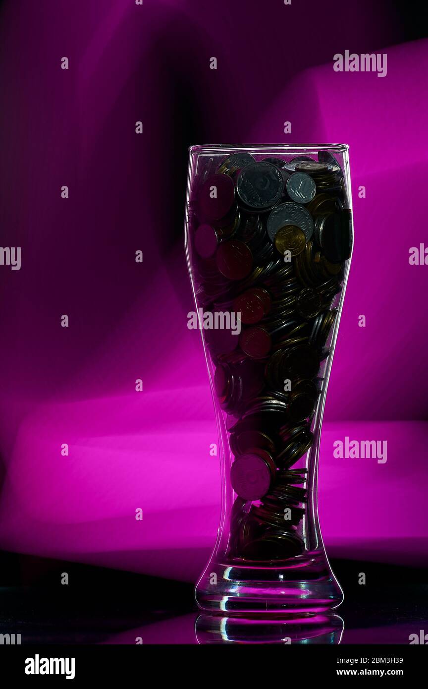 bicchiere di birra pieno di monete su sfondo nero con retroilluminazione Foto Stock