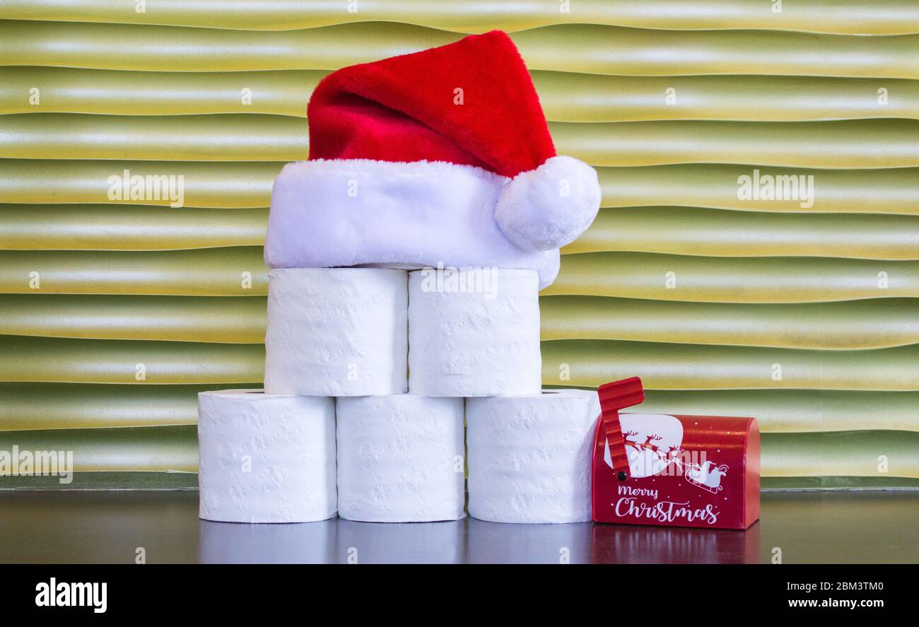 Rotoli di carta igienica con un cappello di Babbo Natale rosso e bianco  sulla parte superiore, accanto ad una piccola mailbox di Natale, su uno  sfondo d'oro con spazio per le copie
